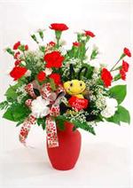 Red glass vase filled with both large and mini red and white carnations, mixed greenery, with valentine ribbons and sitting on top a plush 