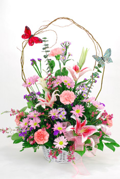 Charming "Butterflies and Blossom filled this wicker basket. Bright pink carnations with lavender daisies, pink roses, purple liatris, yellow solidaster, bells of Ireland, with million star gyp and mixed greens.