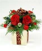 Creamic gift box container filled with red roses, red mini carnations, gold glass ornaments, holly, pine cones with christmas evergreens, baby breath and toped with burgany and gold wired ribbon.