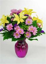 The name says it all, “Harmony”. This richly colored purple glass vase is filled with bright yellow Asiatic lilies, lavender spray dasies, with yellow solid ago, purple statice, and mixed greens. Call today, and you gift of kindness will be on it’s way. 